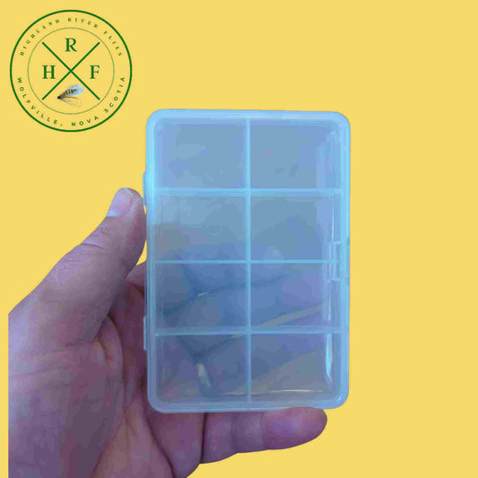 Clear plastic compartmentalized container held in a hand against a yellow background with a logo in the corner.